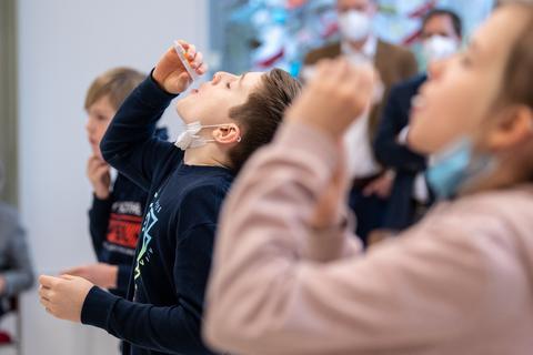 Grundschüler lassen sich während eines selbst durchgeführten Corona-Tests ein Wattestäbchen aus einem Teströhrchen in den Mund fallen.  Foto: dpa