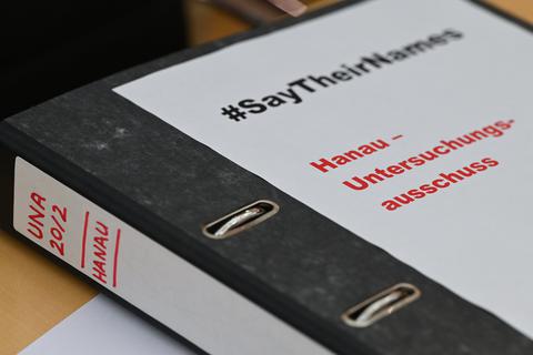 Ein Aktenordner mit der Aufschrift «#SayTheirNames. Hanau-Untersuchungsausschuss» liegt beim Auftakt des Untersuchungsausschusses zum rassistischen Anschlag von Hanau 2020 auf dem Platz einer Abgeordneten der Partei Die Linke.  Foto: Arne Dedert/dpa 